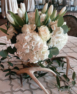 Romantic reception table with a lush floral centerpiece of roses and seasonal greenery